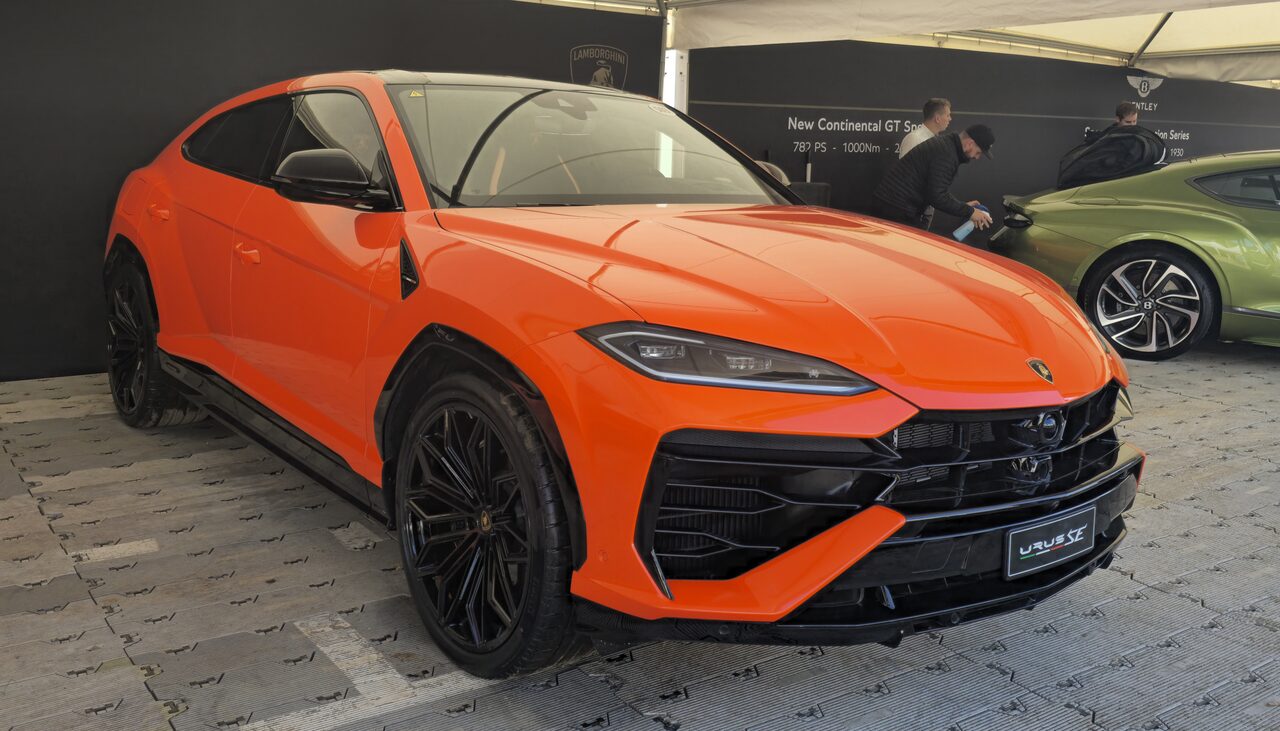 Lamborghini Urus SE laranja exposto num estande, com outro carro verde ao fundo